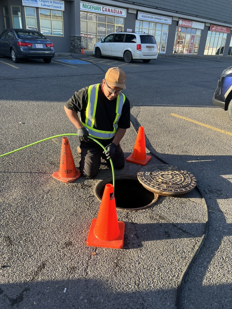 High-pressure jetting hose being fed into a sewer line outside a Calgary business
